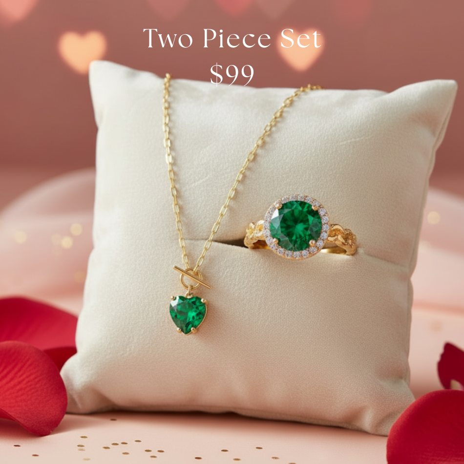 Two-piece emerald jewelry set with necklace and ring on a white pillow with red heart-shaped petals.