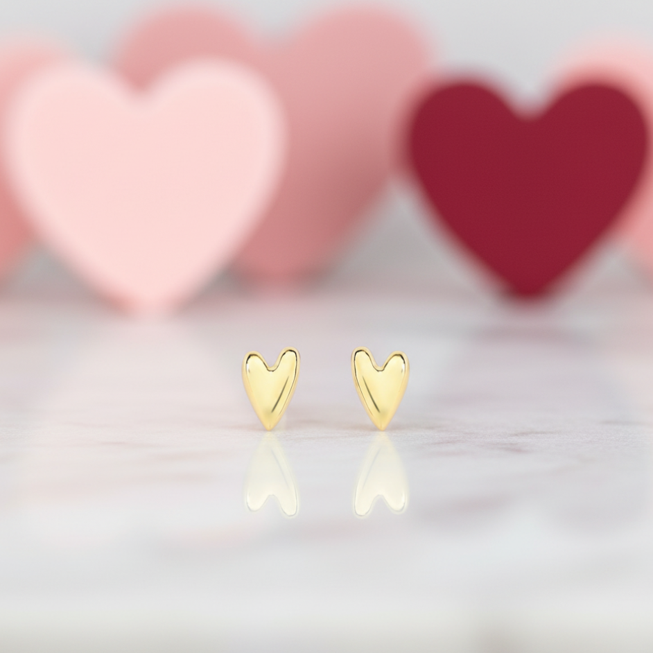 Gold heart-shaped earrings with a soft, blurred heart-patterned background.