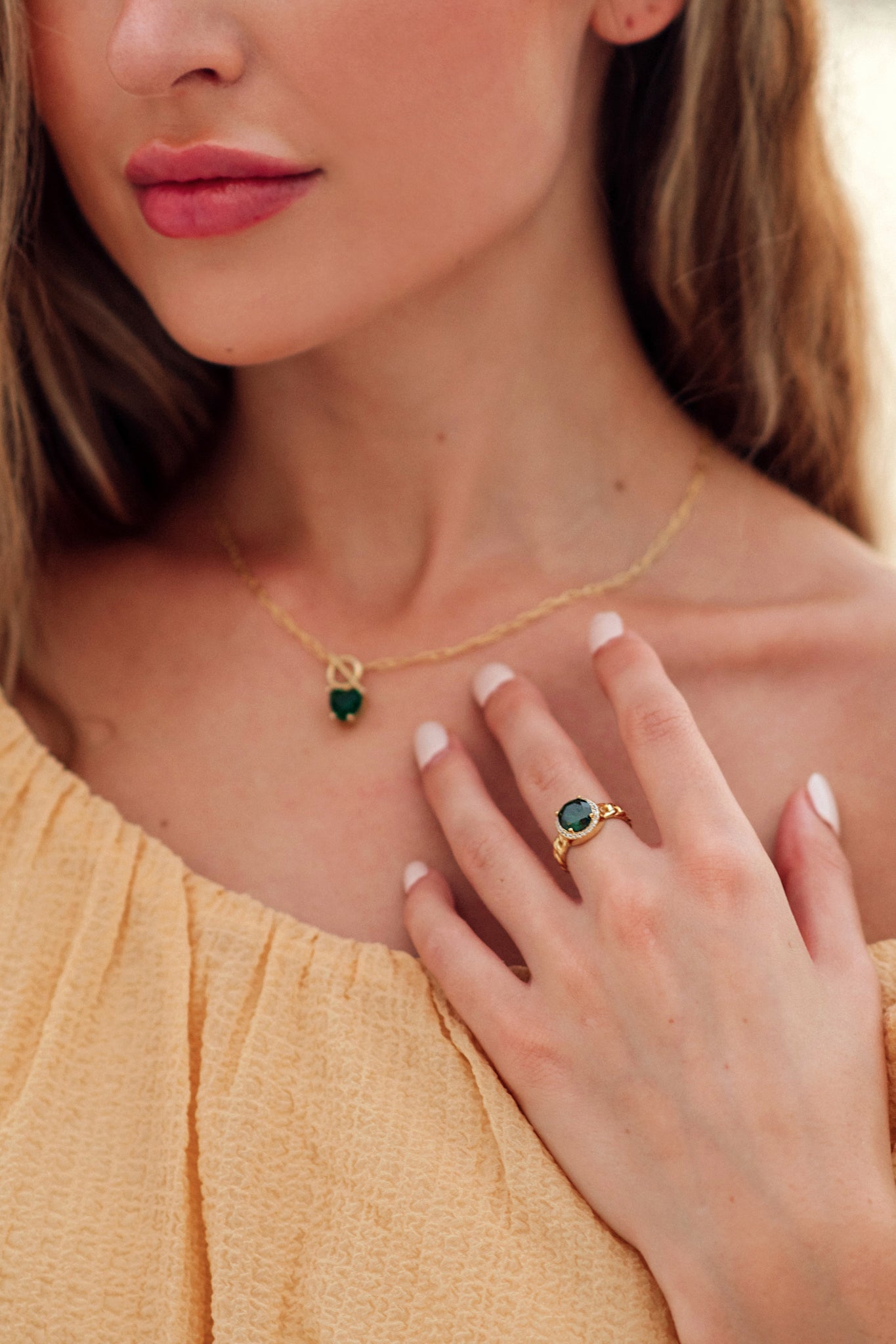 Close-up of a woman wearing a gold necklace and ring with a green gemstone.