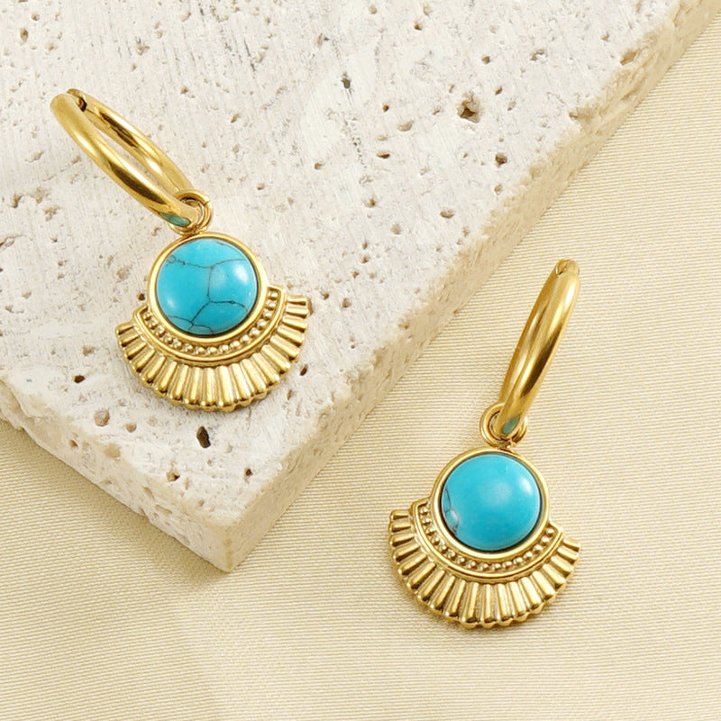 Gold earrings with turquoise stones on a textured beige surface