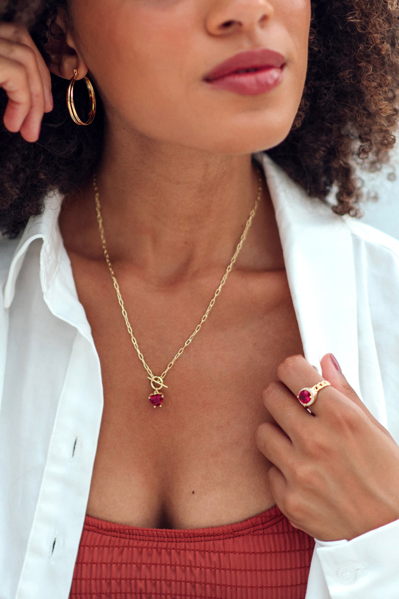 Woman wearing a gold necklace with a red pendant and matching ring.