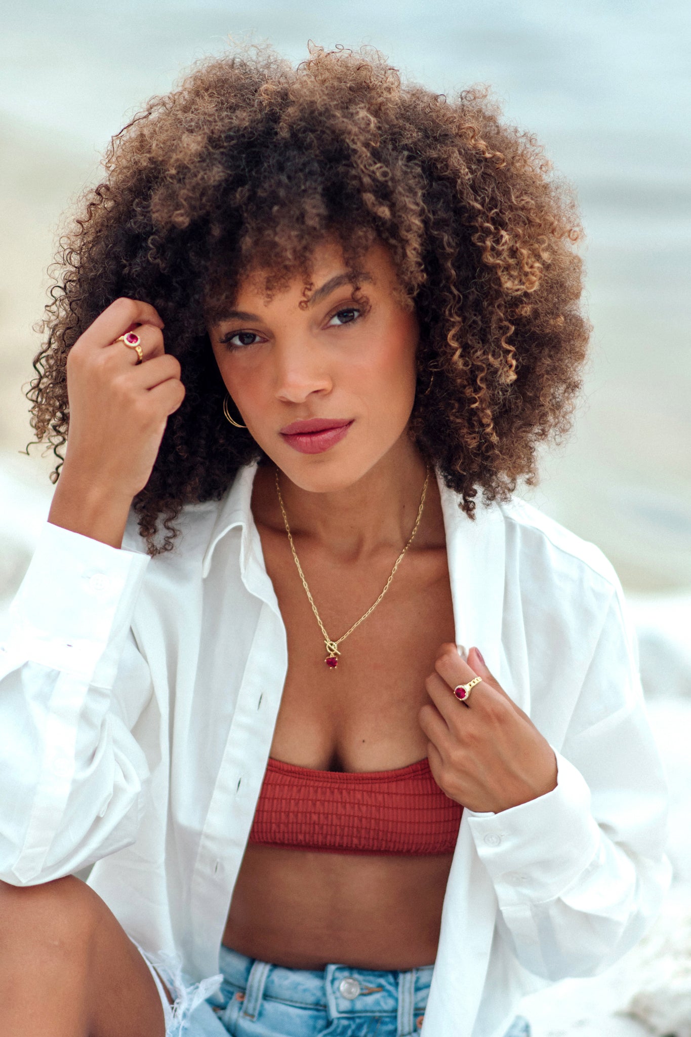 Woman with curly hair wearing a white shirt over a red top and blue jeans.