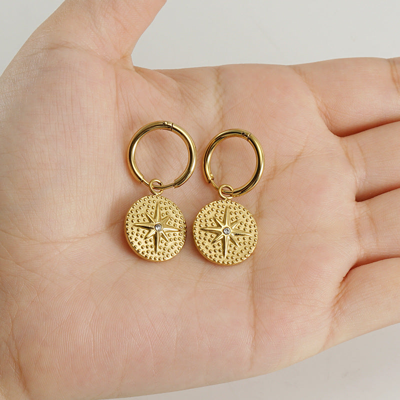 Close-up of Elba gold hoop earrings featuring six-point star pendant with white stone